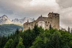 Schloss Naudersberg ragt aus einer Baumsilhouette heraus, im Hintergrund ein Bergkamm