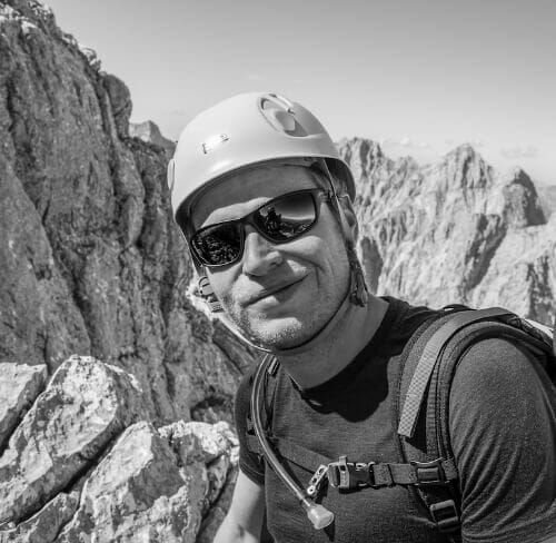 schwarz/weis Peakture Portraitfoto von einem Mann auf einem Klettersteig. Berge im Hintergrund