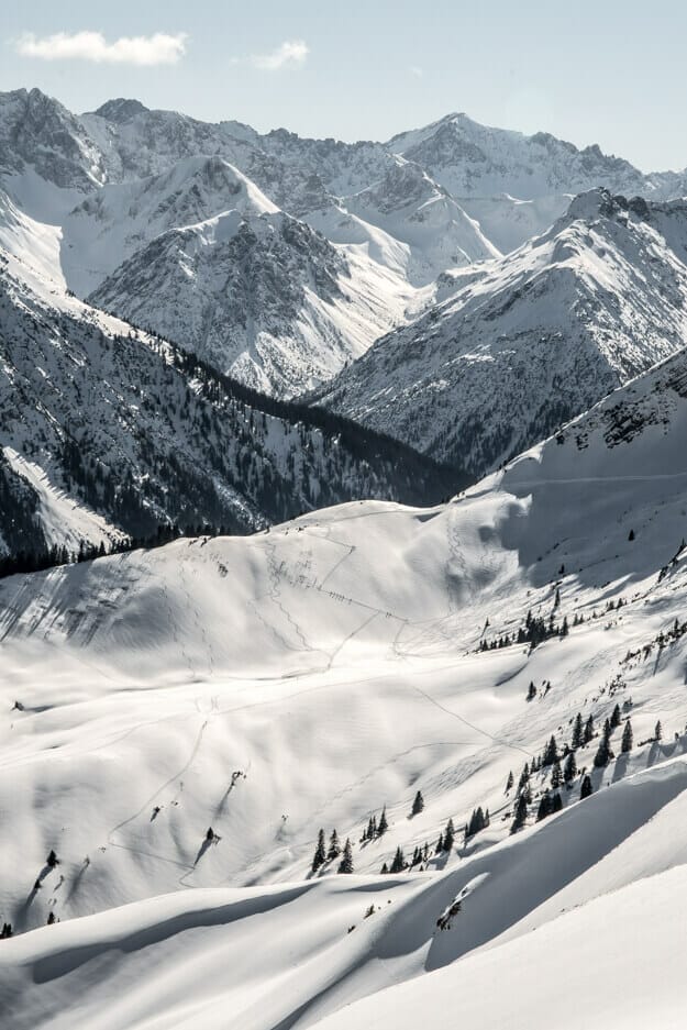 sehr schöner Blick in das umliegende Bergpanorama. Eine weiße Winterlandschaft mit vereinzelten Bäumen.