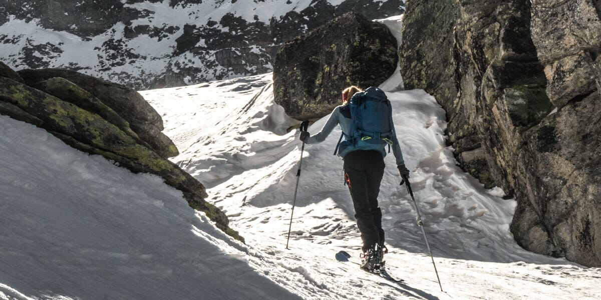 Frau mit Ski durch eine Felsformation beim Aufstieg zum Sillingkopf
