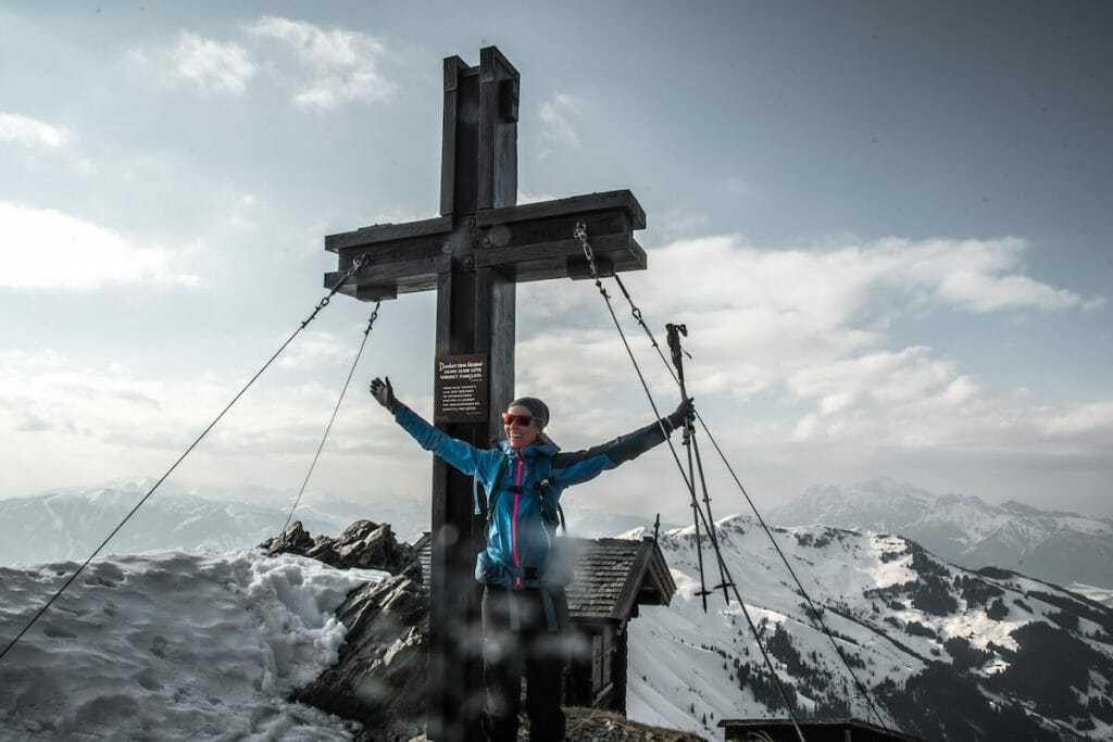 Frau freut sich als sie am Gipfel des Hundsteines angekommen ist. Im Hintergrund eine kleine Hütte und das Gipfelkreuz