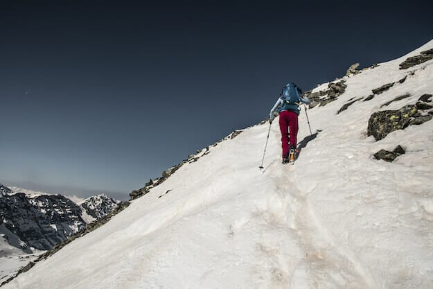 Frau auf Bergtour mit Ski, sie läuft quer zum schneebedeckten Hang