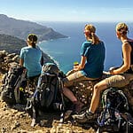 drei hübsche Frauen bei einer kurzen Rast auf dem Trockenmauerweg von Mallorca, im Hintergrund das Meer